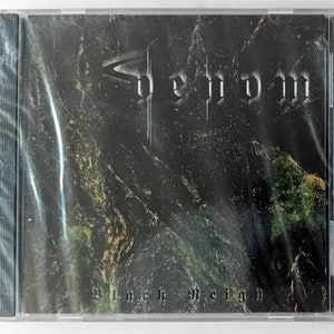 以下が含まれることがあります： 上部にゴシック体の「Venom」という文字が書かれたCDケース。アルバムタイトル「Black Reign」が下にあります。背景は、緑と黒の色合いの暗いテクスチャパターンです。