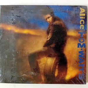 Könnte beinhalten: Ein Vintage-Albumcover mit einem Mann in einer Lederjacke, der auf einem Reifen vor einem Sonnenuntergang sitzt. Der Albumtitel "Alice Tom Waits" ist in Blau auf der rechten Seite des Covers gedruckt.