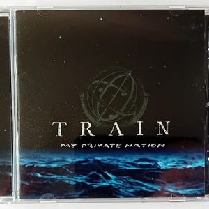 Op de afbeelding: Een cd-hoesje met het album "My Private Nation" van de band Train. De hoes heeft een donkerblauwe en zwarte achtergrond met een wereldbolontwerp en de bandnaam in het wit. De onderkant toont een blauwe oceaan.
