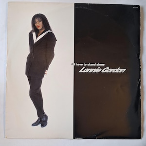 Può includere: Una copertina di un disco in vinile con una persona dai capelli scuri che indossa un blazer nero con risvolti bianchi e pantaloni neri. Il testo recita if i have to stand alone e Lonnie Gordon. Lo sfondo è diviso verticalmente in bianco e nero.