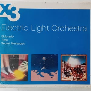 May include: A blue and white album cover with the text "Electric Light Orchestra" and the album titles "Eldorado", "Time", and "Secret Messages". The cover features three images of album covers: a red shoe on a yellow background, a blue and pink planet with a star field, and a city scene with a bright light in the sky.