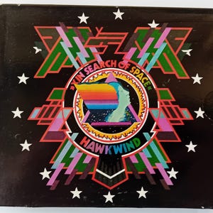May include: A black and white album cover with a colorful circular design in the center. The design features a rainbow-colored wing, a star-filled sky, and the text "In Search of Space". The album title "Hawkwind" is written in a bold, stylized font below the circular design.