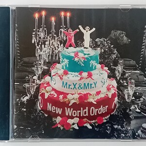 May include: A three-tiered cake decorated with red, white and blue icing. The cake is topped with two figures, one in red and one in white. The cake is surrounded by candles, glasses and a black tablecloth. The cake is labelled "Mr. X & Mr. Y" and "New World Order".