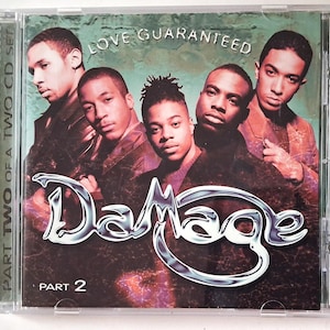 Op de afbeelding: Een muziek-cd-hoesje met de groep Damage met de tekst Love Guaranteed en Part 2. De hoes toont vijf personen in donkere kleding tegen een getextureerde groene en zwarte achtergrond met een metallic zilveren logo voor de bandnaam.