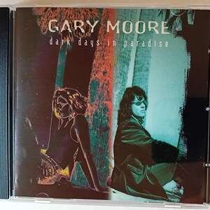 以下が含まれることがあります： 黒い背景に2人の人物の写真が写っているCDケース。ケースには「Gary Moore dark days in paradise」という文字が書かれている。