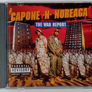 Op de afbeelding: Een CD-hoes met een rood, wit en zwart ontwerp. De titel van het album is "Capone-N-Noreaga: The War Report". De albumhoes toont twee mannen in camouflagekleding die voor een stadsgebouw staan. Een waarschuwing voor ouders staat in de linkerbenedenhoek.