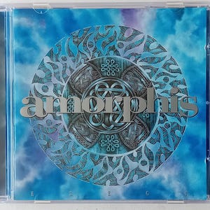 May include: A CD case with a blue and purple background featuring a silver Celtic knot design. The band name "AMORPHIS" is written in silver letters across the design. The album title "ELEGY" is written in silver letters at the bottom of the case.