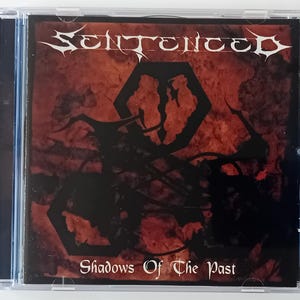 May include: A CD case with a red and black design. The front cover features the band name "SENTENCED" in white lettering and the album title "Shadows Of The Past" in white lettering.