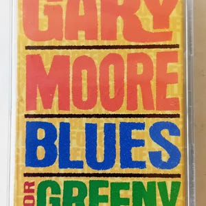 以下が含まれることがあります： 赤い、ピンク、青、緑の文字で「GARY MOORE BLUES FOR GREENY」と書かれた黄色のカセットテープです。