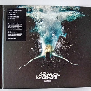 Puede incluir: Caja de CD de "The Chemical Brothers - Further: The Deluxe Edition". La portada muestra a una persona buceando en el agua, con el nombre de la banda y el título del álbum en blanco. Una etiqueta en la esquina superior izquierda detalla el álbum.