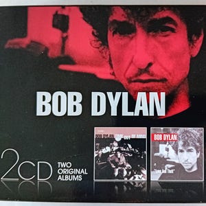May include: A two-disc CD set featuring Bob Dylan. The front cover features a close-up of Bob Dylan's face. The back cover shows the album covers for "Time Out of Mind" and "Love and Theft".