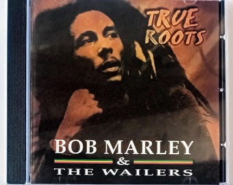 Może przedstawiać: Pudełko CD z wizerunkiem Boba Marleya i tytułem albumu "True Roots". Nazwa artysty, "Bob Marley & The Wailers", jest wyświetlana poniżej. Okładka ma ciemną, ciepłą paletę kolorów.