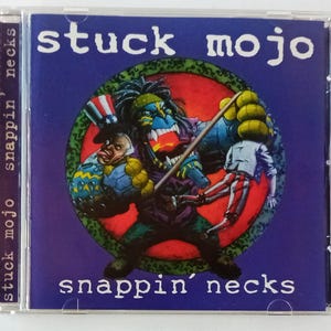 Może przedstawiać: Pudełko CD z albumem "Snappin' Necks" zespołu Stuck Mojo. Okładka przedstawia potworną postać z niebieską twarzą i zielonymi włosami, trzymającą kij i marionetkę. Tytuł albumu i nazwa zespołu są w białym kolorze.