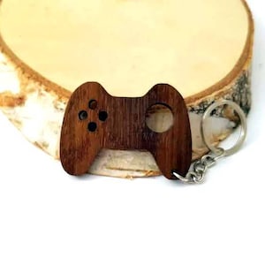 Op de afbeelding: Een houten gamecontroller sleutelhanger met een bruine afwerking. De sleutelhanger is bevestigd aan een zilveren metalen ring en ketting.