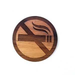 Peut inclure: Un panneau rond en bois avec un symbole d'interdiction de fumer. Le symbole est une ligne diagonale traversant une cigarette avec de la fumée qui s'en échappe.