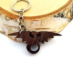 Può includere: Un portachiavi in legno a forma di drago con un anello portachiavi argentato. Il drago è marrone scuro e presenta un design dettagliato.