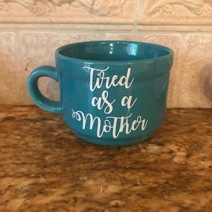 May include: Teal ceramic mug with white text that reads "Tired as a Mother".