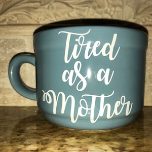 May include: A blue ceramic mug with a white inscription that reads "Tired as a Mother".