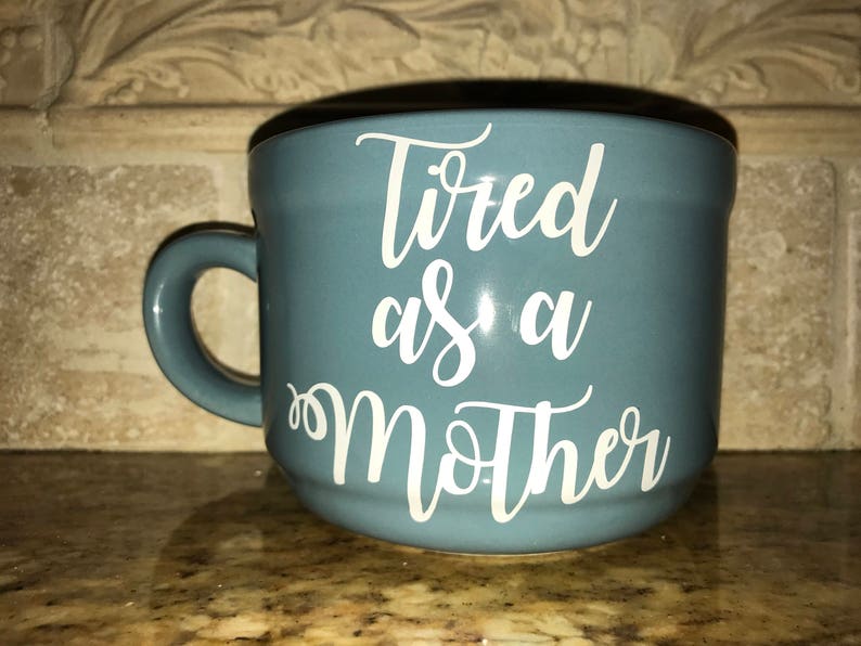 May include: A blue ceramic mug with a white inscription that reads "Tired as a Mother".