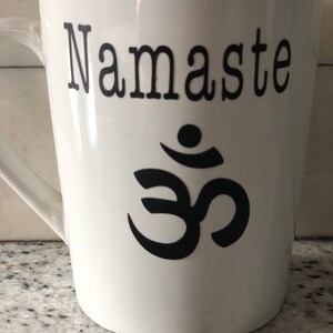 May include: White ceramic mug with a black Om symbol and the word "Namaste" printed on it.