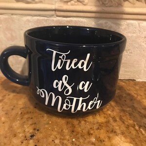 May include: A dark blue ceramic mug with white lettering that reads "Tired as a Mother".