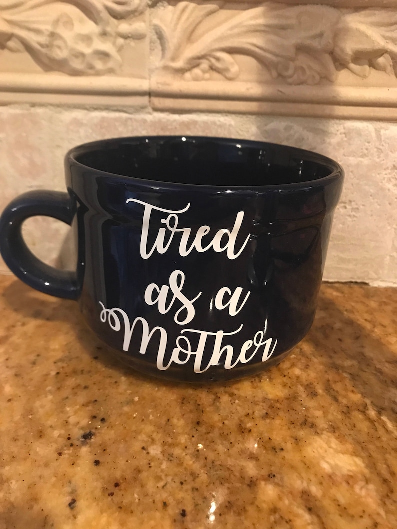 May include: A dark blue ceramic mug with white lettering that reads "Tired as a Mother".