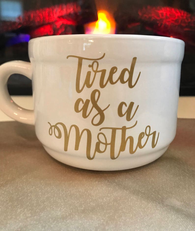 May include: White ceramic mug with a gold inscription that reads "Tired as a Mother".