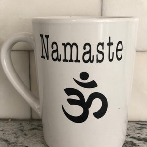 May include: White ceramic coffee mug with a black "Namaste" inscription and a black Om symbol.