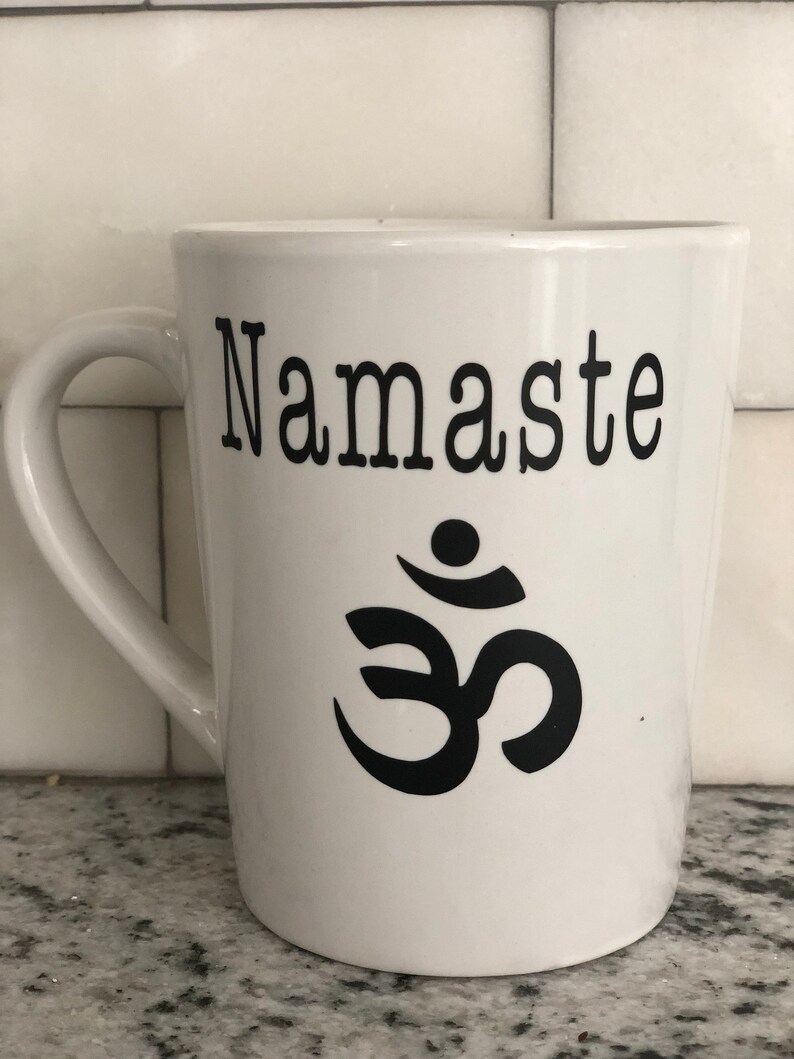 May include: White ceramic coffee mug with a black "Namaste" inscription and a black Om symbol.