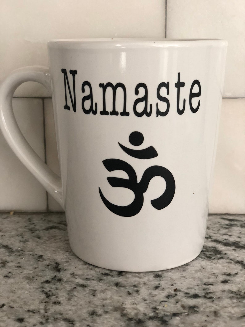 May include: White ceramic mug with a black inscription that reads "Namaste" and a black Om symbol.
