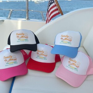 May include: A collection of trucker hats in various colors, including black, red, pink, light blue, and pink. Each hat features a white front panel with the word "Family" and a tropical graphic, along with the text "Cancun 2020". An American flag waves in the background.