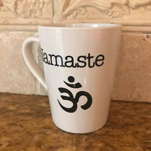 May include: White ceramic mug with a black "Namaste" and Om symbol graphic.
