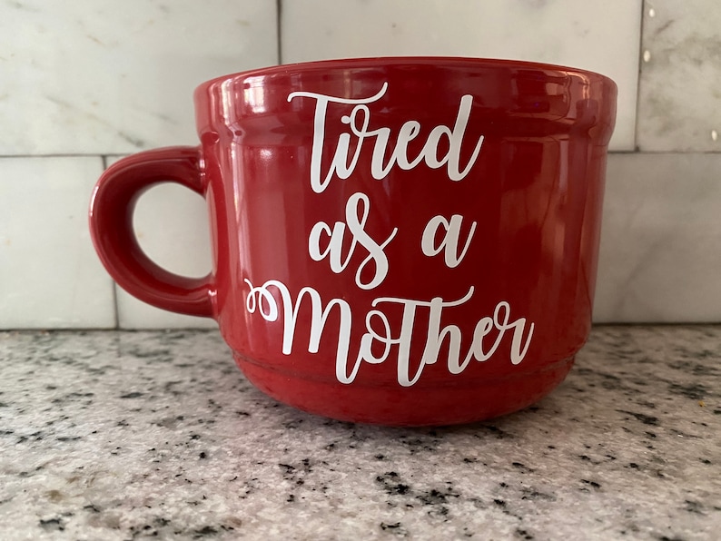 May include: Red ceramic coffee mug with a white inscription that reads "Tired as a Mother".