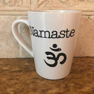 May include: White ceramic coffee mug with a black "Namaste" inscription and an Om symbol.