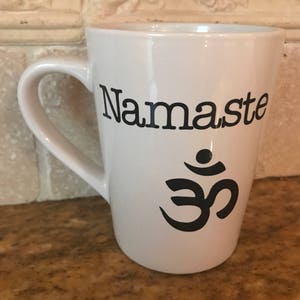 May include: White ceramic coffee mug with a black "Namaste" inscription and a black Om symbol.