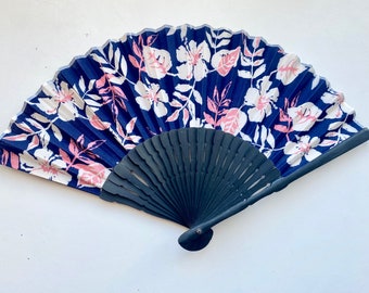 May include: A blue and white floral hand fan with a black wooden handle. The fan is closed and has a pink floral pattern.