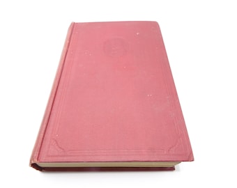 May include: A red hardcover book with a decorative design on the front cover. The book is closed and lying flat on a white surface.