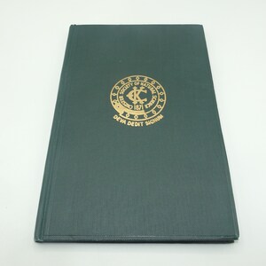 Puede incluir: Un libro de tapa dura de color verde oscuro con un sello en relieve dorado en la portada. El sello presenta el texto "Society of Natural Science" y "Deva Deddit Signum".