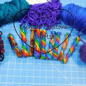 May include: A collection of eight handcrafted crochet hooks with spiral rainbow-coloured patterns and natural wood accents, arranged horizontally. The text 'Dunlap Custom Crafts' is centred over the hooks, surrounded by various skeins of yarn.