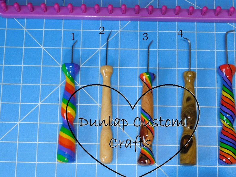 Peut inclure: Cinq crochets de m&eacute;tier &agrave; tisser en m&eacute;tal avec des manches d&eacute;coratifs, dont trois avec des motifs arc-en-ciel et deux avec des finitions en bois naturel. Les crochets sont num&eacute;rot&eacute;s de un &agrave; quatre, avec le texte Dunlap Custom Crafts en forme de c&oelig;ur.