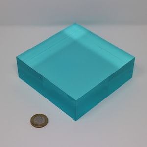 Könnte beinhalten: Ein quadratischer, durchsichtiger, türkisfarbener Acrylblock. Der Block ist etwa 7,5 cm groß.