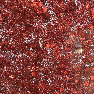 May include: A close-up of red glitter, with a white background. The glitter is in various shapes and sizes, and it is very sparkly.