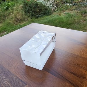 May include: A clear, rectangular, glass paperweight with a textured surface. The paperweight is sitting on a wooden table.