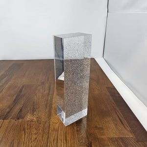 May include: A clear glass block with a sparkly silver glitter finish. The block is rectangular and has a smooth surface.