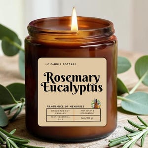 May include: A lit brown glass jar candle with a label that reads "Rosemary Eucalyptus." The label also states "Handmade Soy Candles" and "100% Essential Oils." The candle is 9oz/252 gr and is surrounded by green leaves.