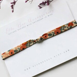 May include: A white card with the text "Elle Bee Accessories" and "Refined Designs with Childhood in Mind." A floral patterned fabric hair tie is tied around the card. The text "www.ellebee.etsy.com" is printed on the bottom of the card.