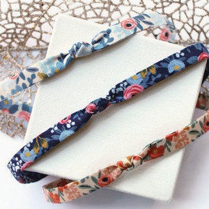 May include: Three fabric headbands with knotted ends. The headbands are in floral patterns with blue, pink, and white flowers on a navy blue, beige, and white background.