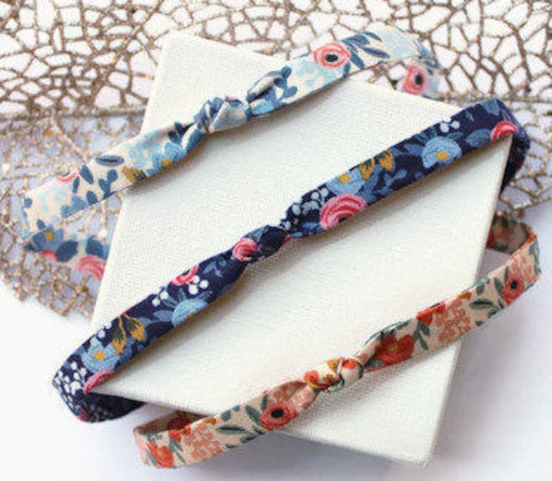 May include: Three fabric headbands with knotted ends. The headbands are in floral patterns with blue, pink, and white flowers on a navy blue, beige, and white background.