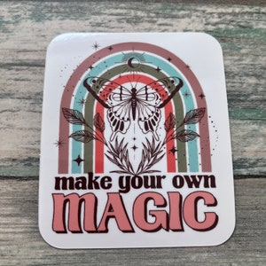 May include: A white sticker with a rainbow, a butterfly, and the text "make your own MAGIC" in pink and brown letters.