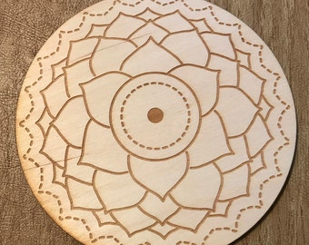 May include: A wooden mandala with a flower design and a circle in the center. The mandala is engraved with a pattern of lines and dots.